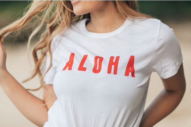 Close up of Aloha printed on white t-shirt in red ink, women wearing it playing with hair
