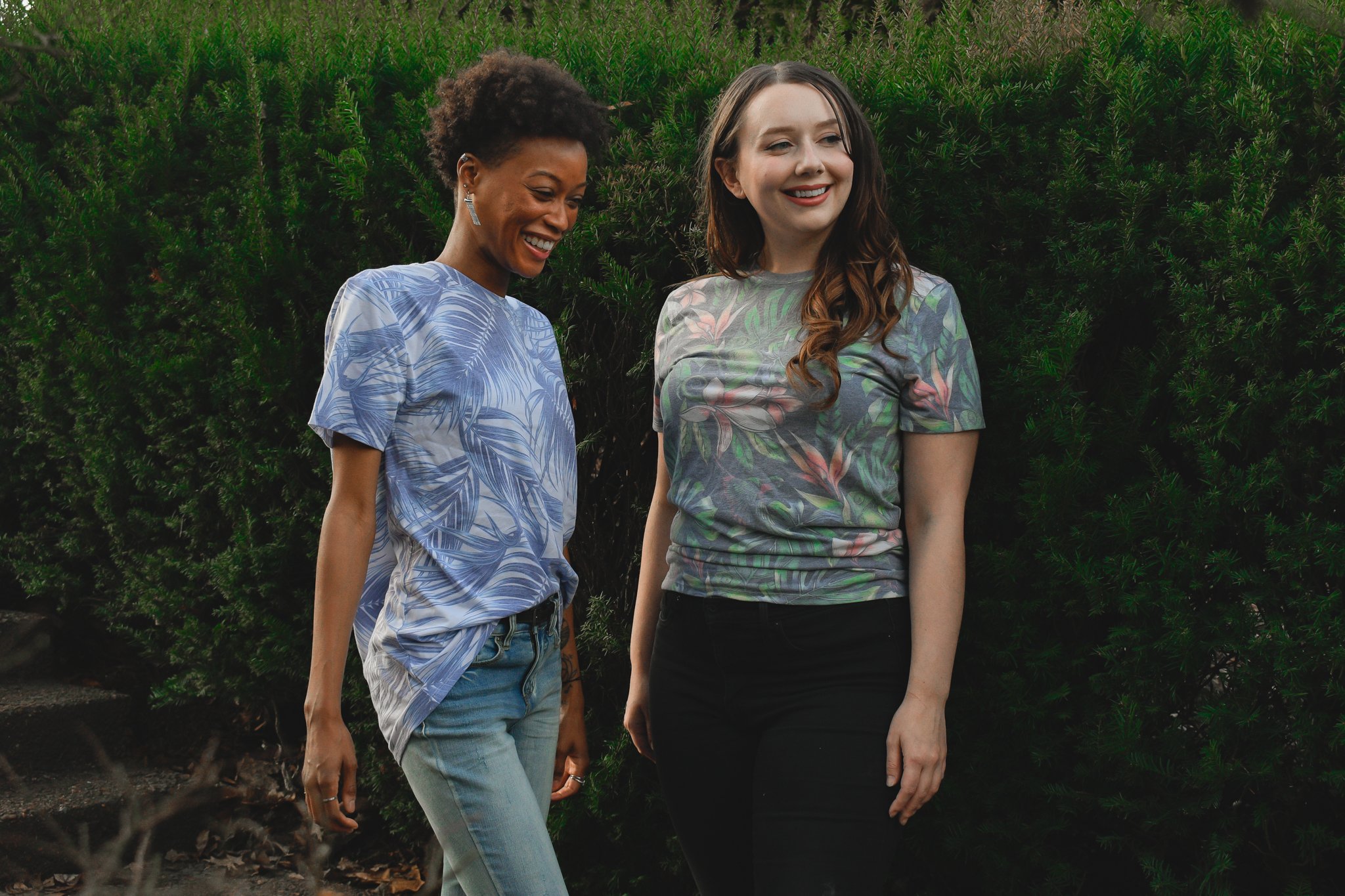 Two women wearing printed t-shirts from threadfast featuring tropical themed prints all over the garment 