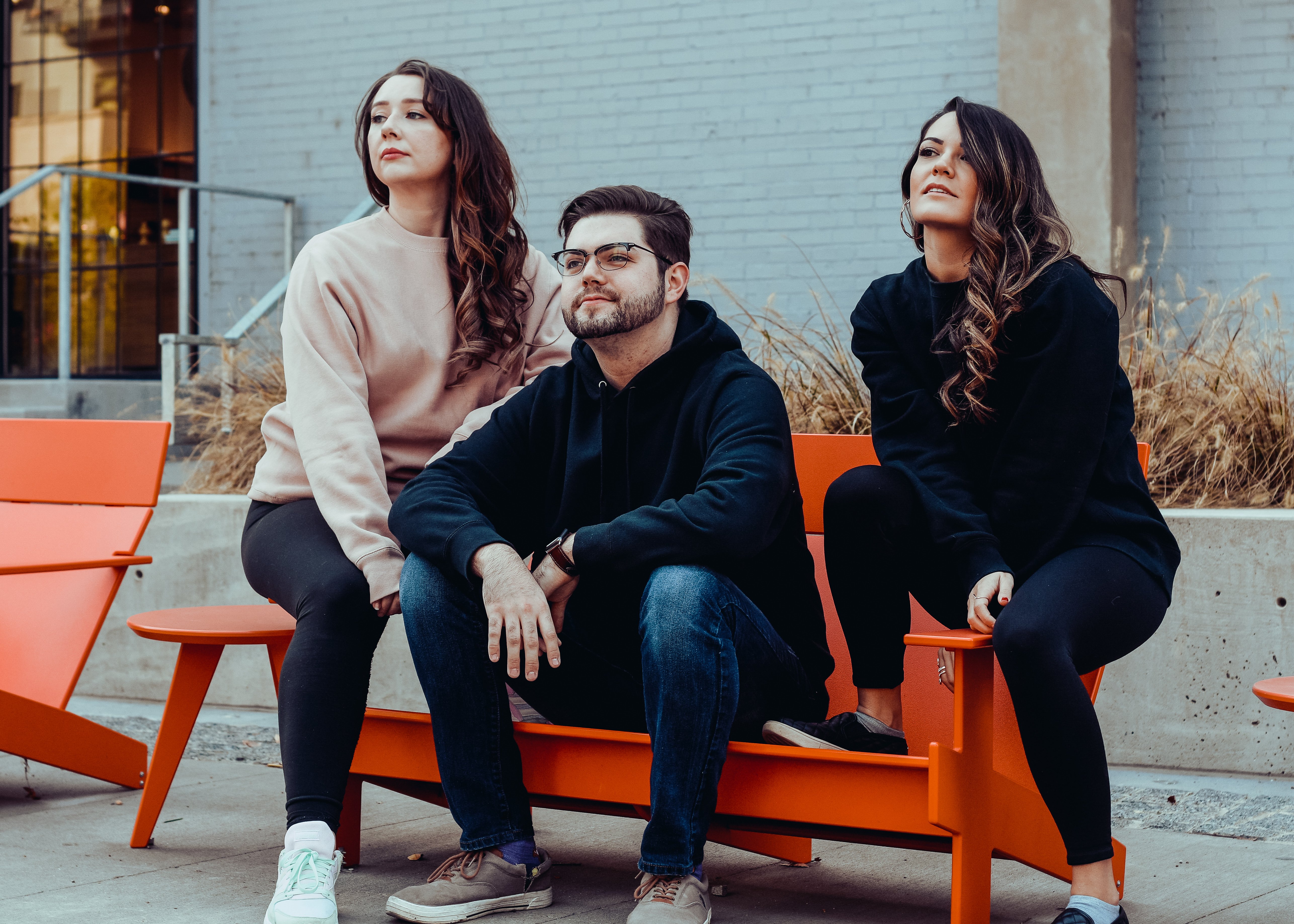 Three people sitting on bench wearing hoodies and sweatshirts from ITC