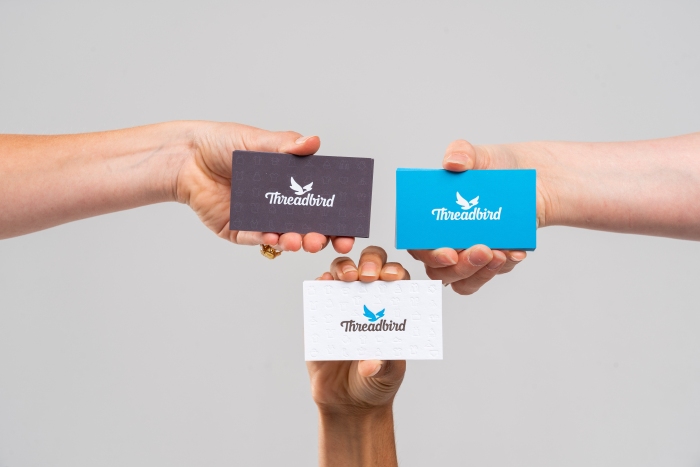 Blue, Grey, and White Threadbird business cards all being held by different hands