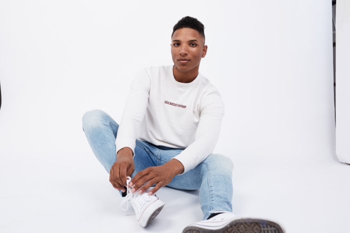 'In Search of Hip Hop' embroidered on a white sweatshirt worn by a model sitting down 
